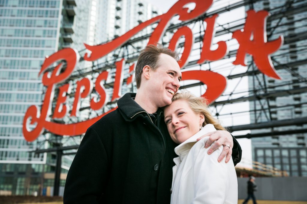 Couple hugging in front of neon Pepsi Cola sign in Gantry Plaza State Park at a Long Island City wedding brunch