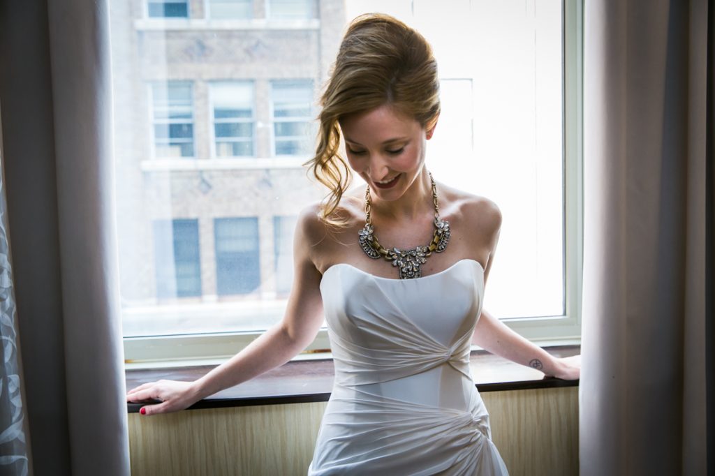 Bride wearing sleeveless wedding dress leaning against window
