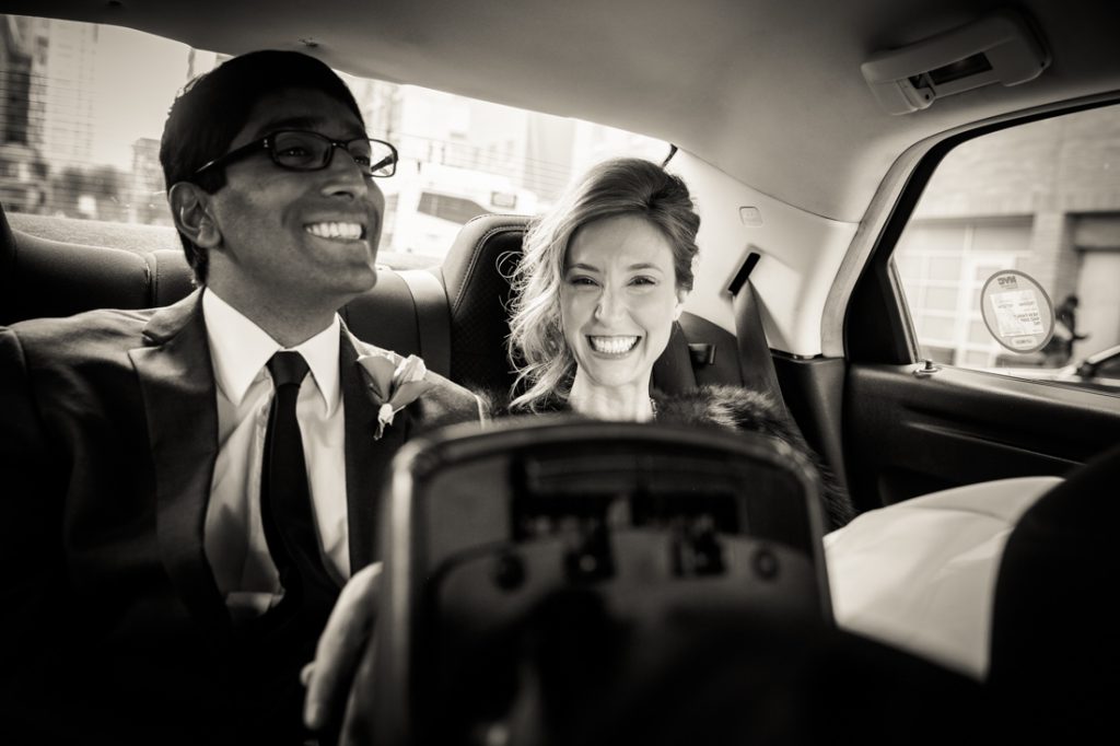 Black and white photo of bride and groom in back of taxi