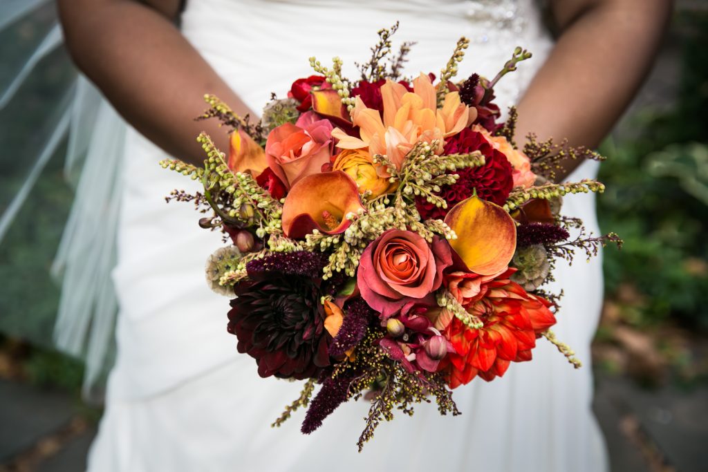 Close up on bride holding bouquet with orange, red, and yellow flowers