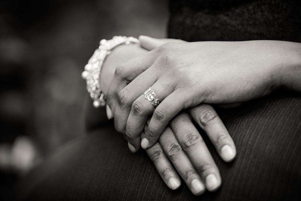 Black and white photo of bride's hands around groom's neck wearing engagement ring