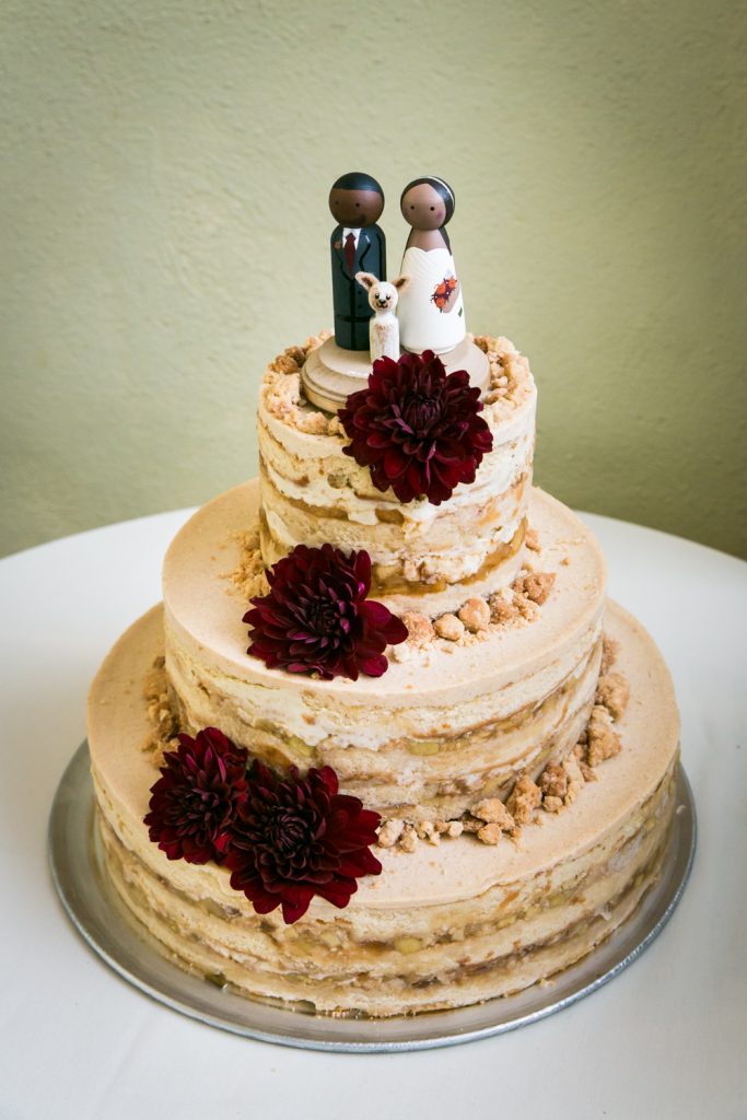 Momofuku milk wedding cake with brown icing, red flowers, and African American toppers