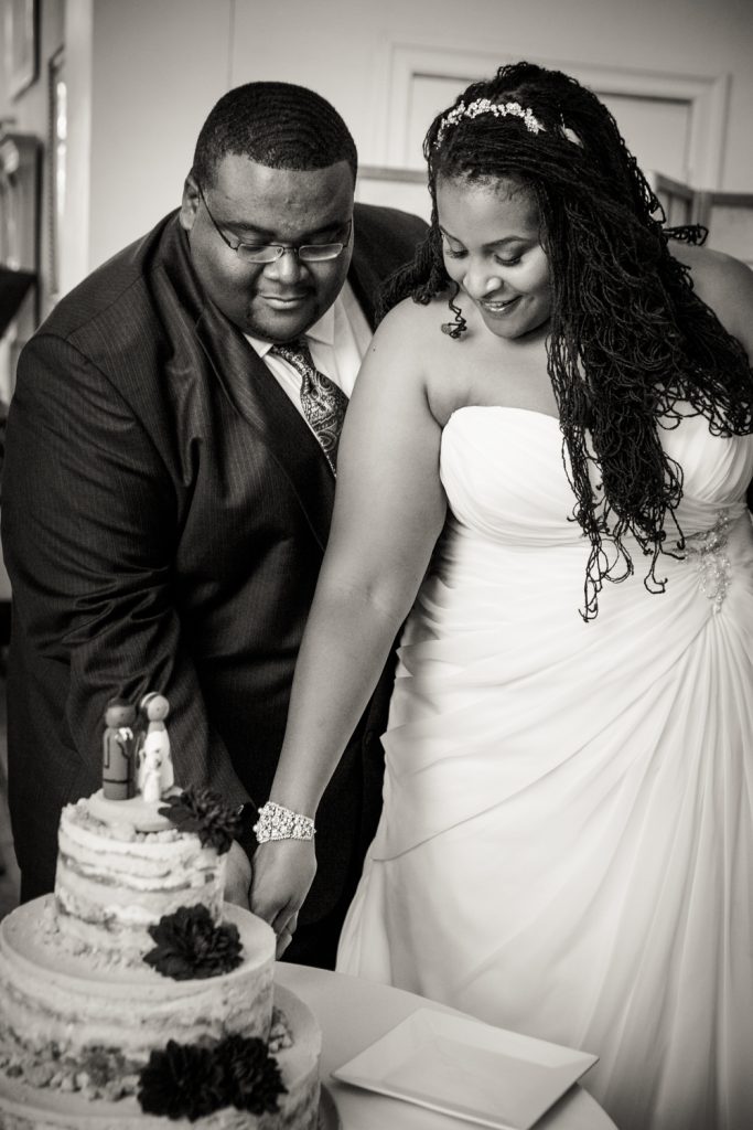 Black and white photo of bride and groom cutting wedding cake