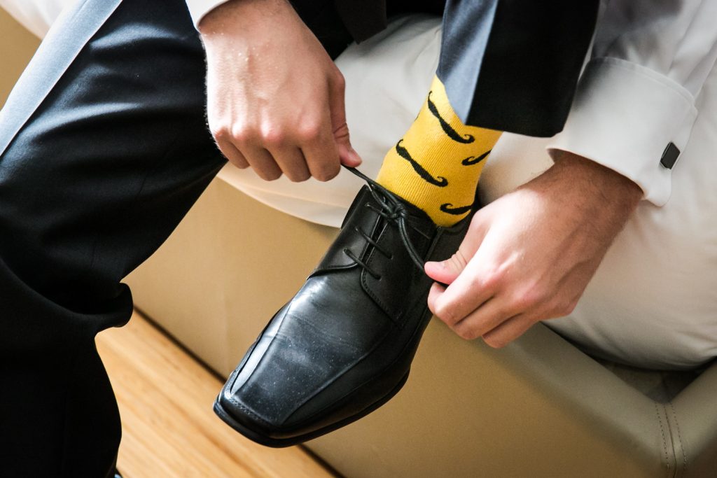 Close up of groom tying black shoe and wearing yellow socks with mustaches 