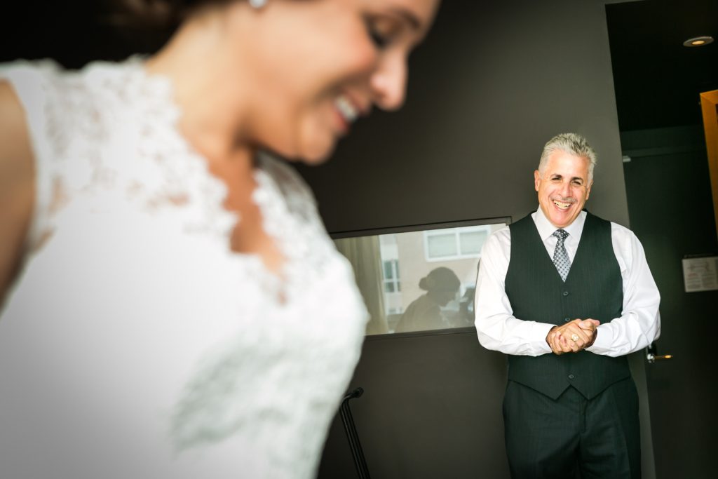 Father of bride watching as bride gets ready in hotel room