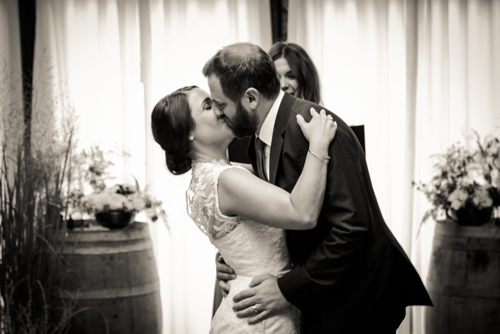 Black and white photo of bride and groom kissing after ceremony