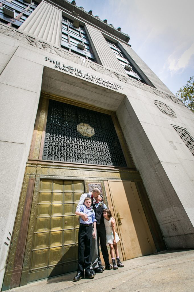 Two grooms and children outside bronze doors after a NYC LGBTQ City Hall wedding