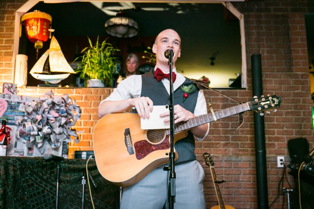 Groom speaking into microphone and holding guitar