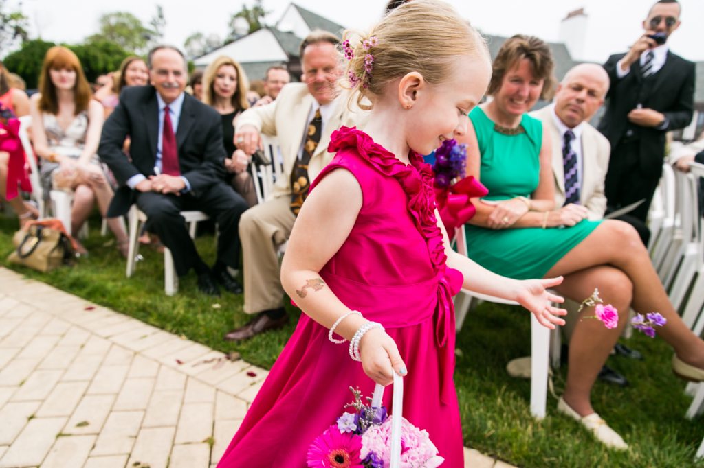 Little flower girl in pink dress throwing flowers down aisle at Riviera Waterfront Mansion wedding