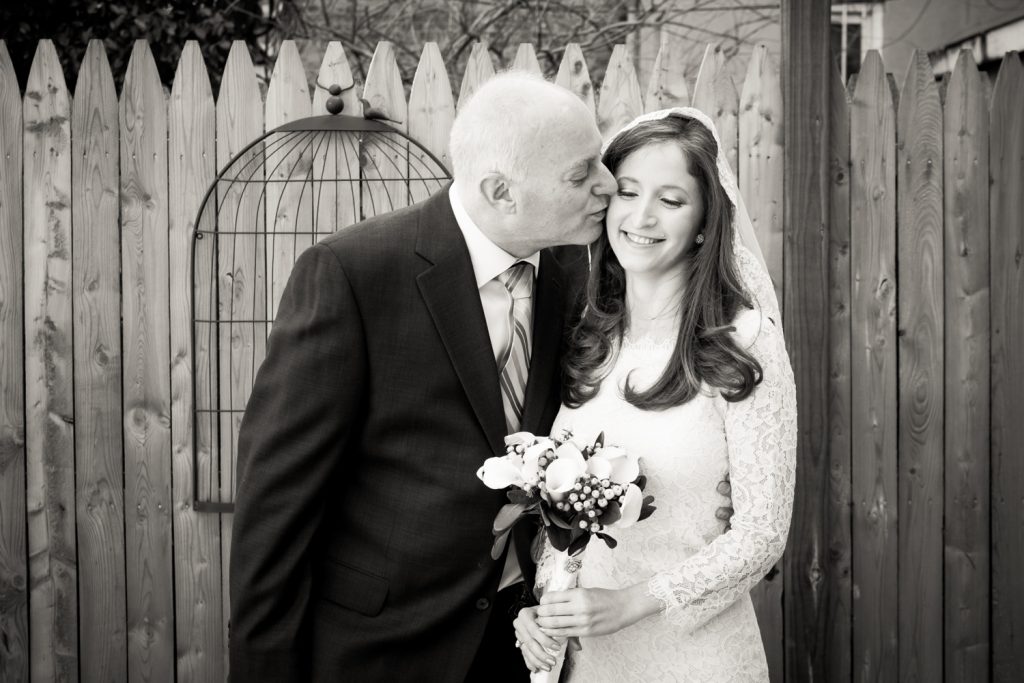 Black and white photo of father kissing bride on side of head