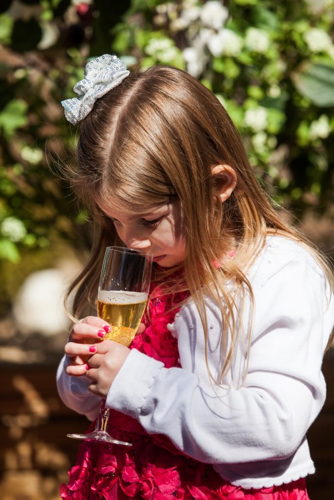 Little girl drinking glass of apple cider in champagne glass