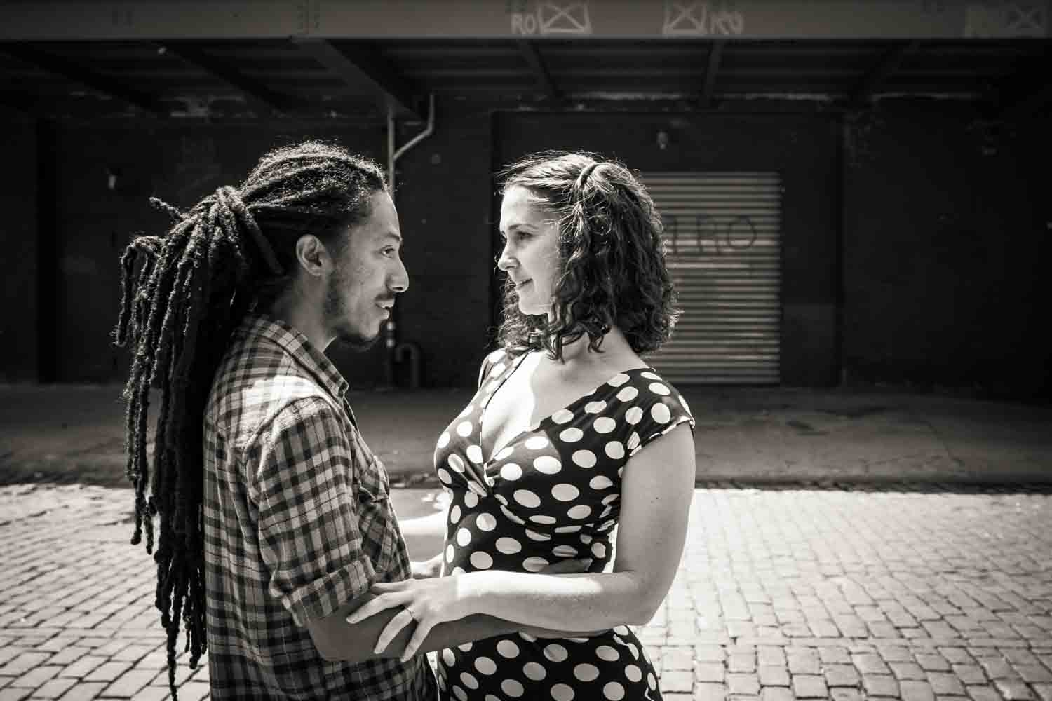 Black and white photo of couple looking at each other in middle of street