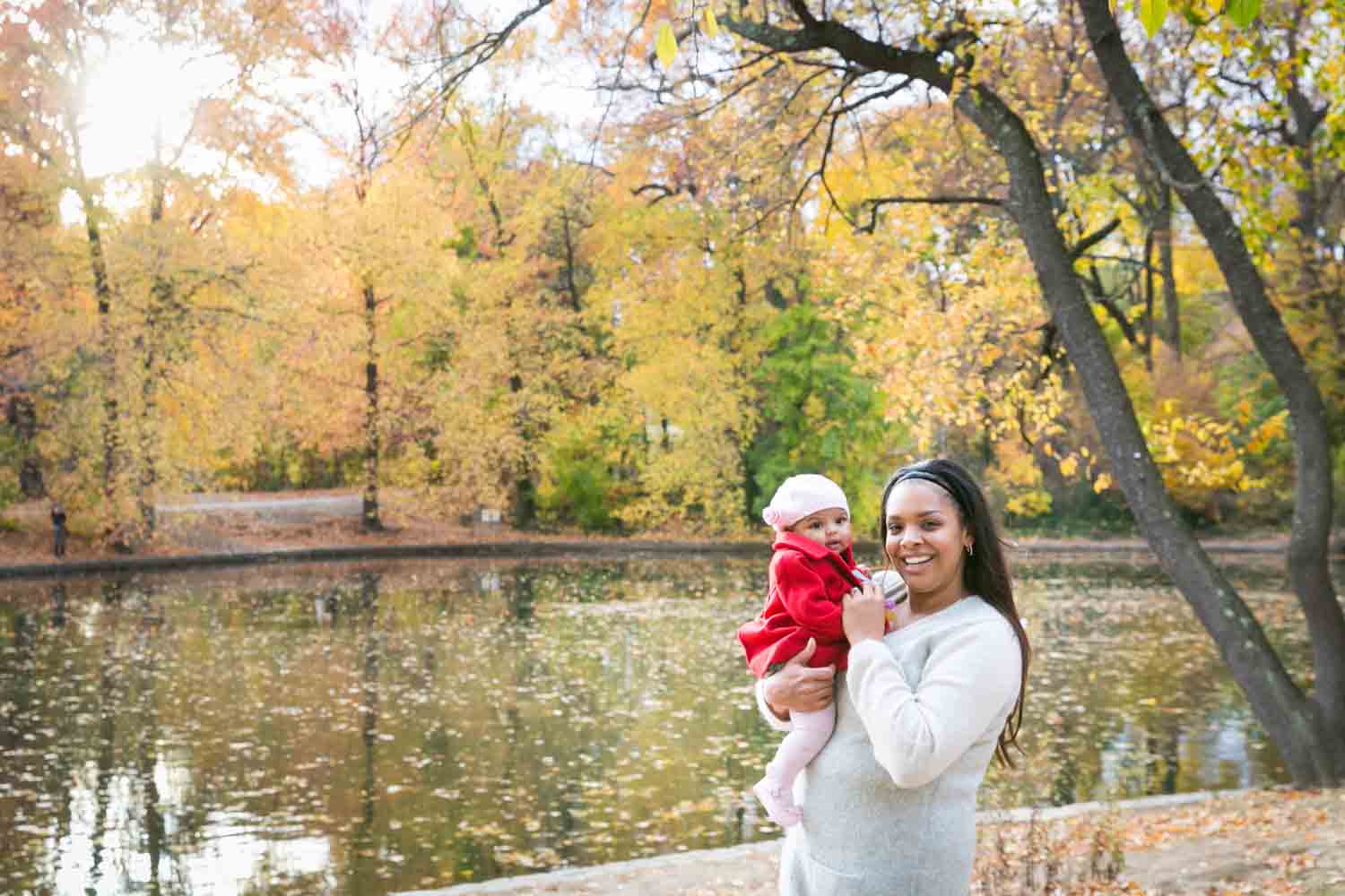 Mother holding baby wearing red coat in front of lake
