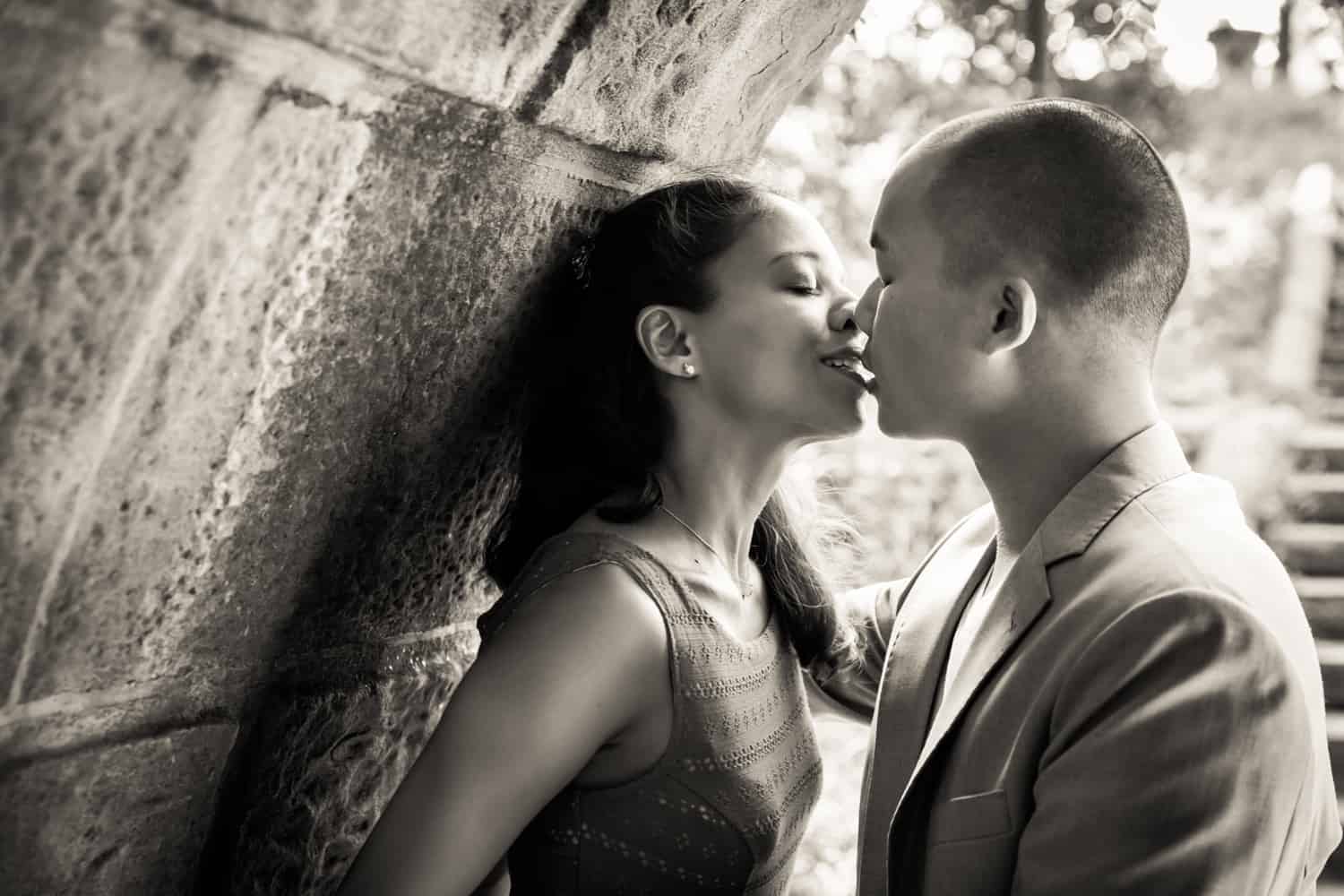 Black and white photo of couple kissing under Trefoil Arch in Central Park
