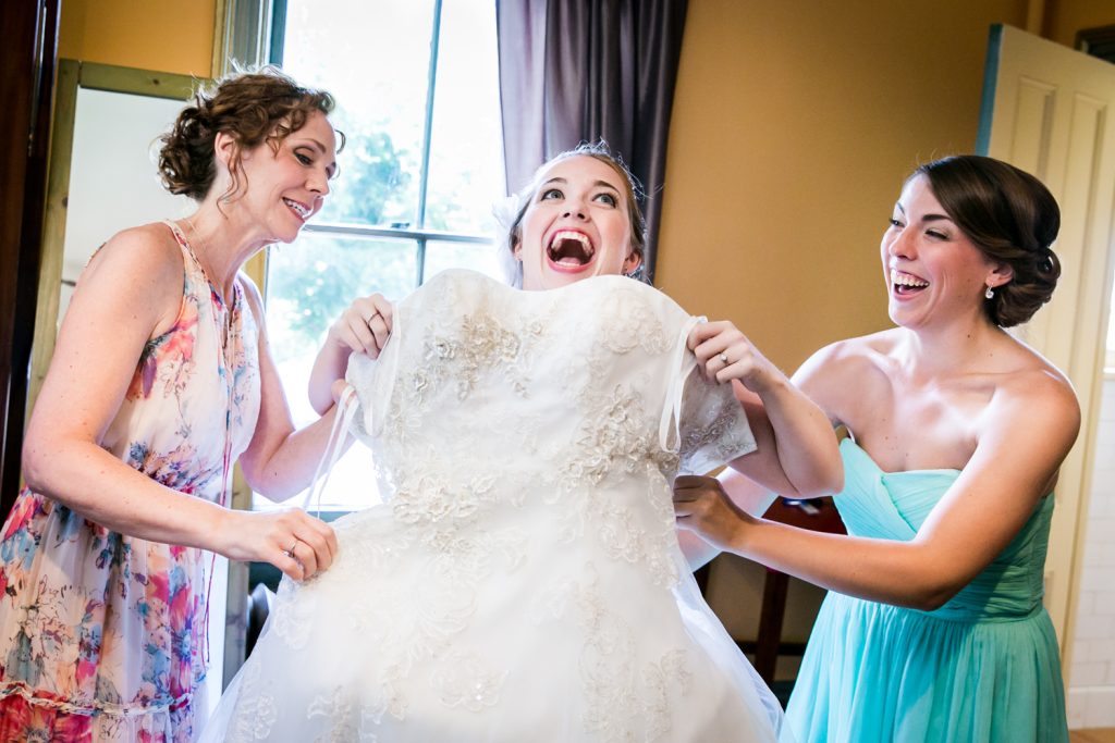 Two women pulling wedding dress on bride at a Round Hill House wedding