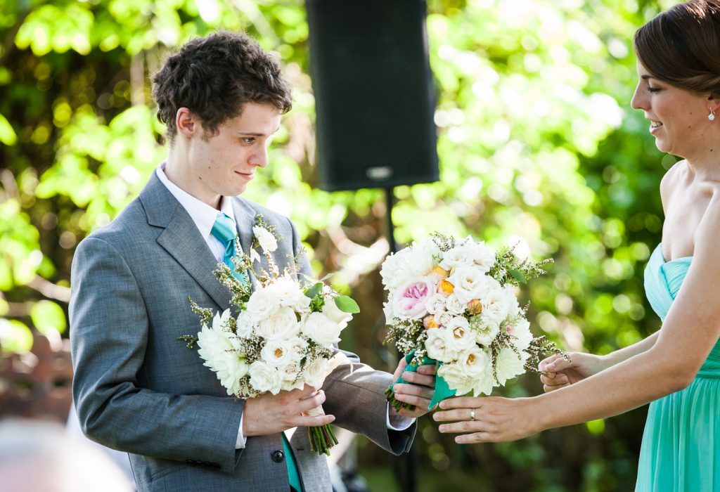 Maid of honor handing bouquets to groomsman at a Round Hill House wedding