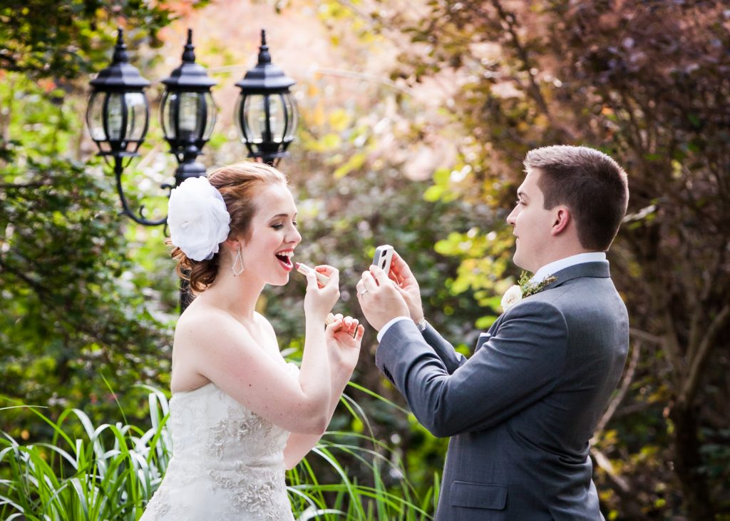 Groom holding mirror for bride who is applying lipstick