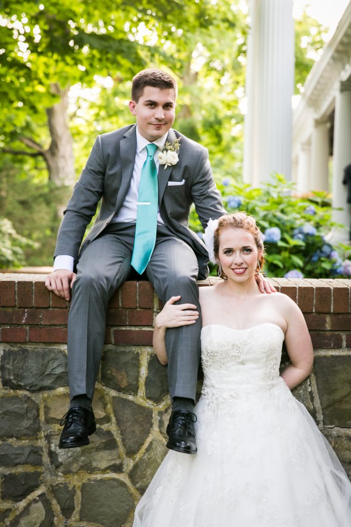 Groom sitting on wall and bride holding leg of groom 