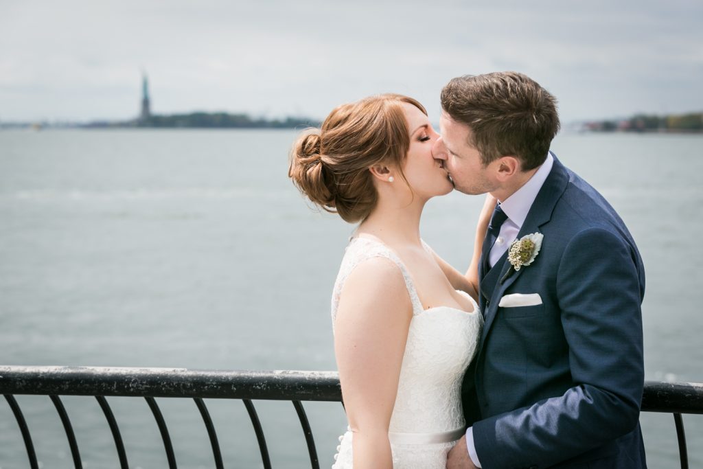 Bride and groom kissing with Statue of Liberty in background
