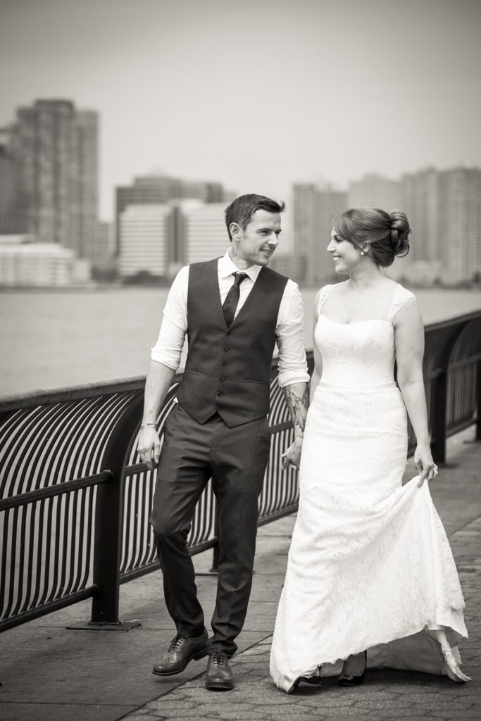 Black and white photo of bride and groom walking along Battery Park