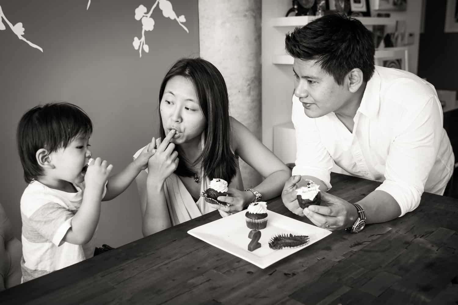 Black and white photo of parents and child eating cupcakes