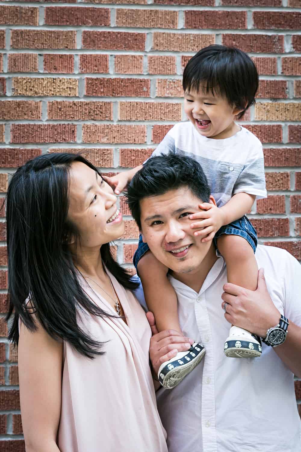 Manhattan family portrait of parents and little boy in front of brick wall