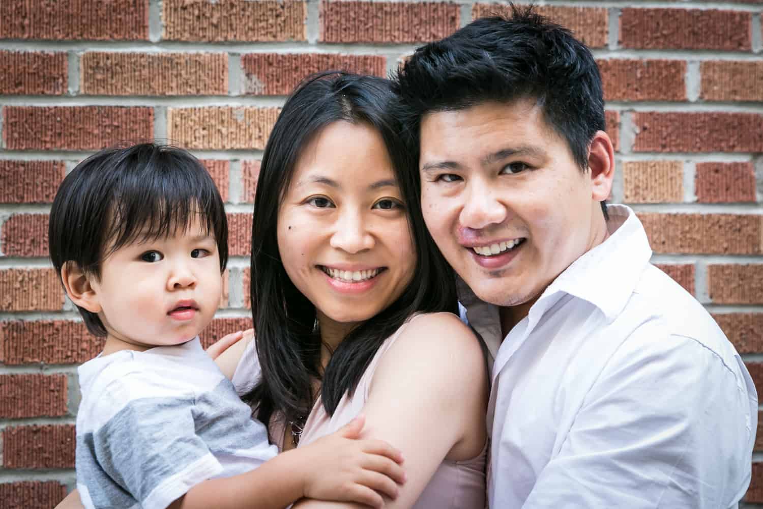 Manhattan family portrait of parents and little boy in front of brick wall