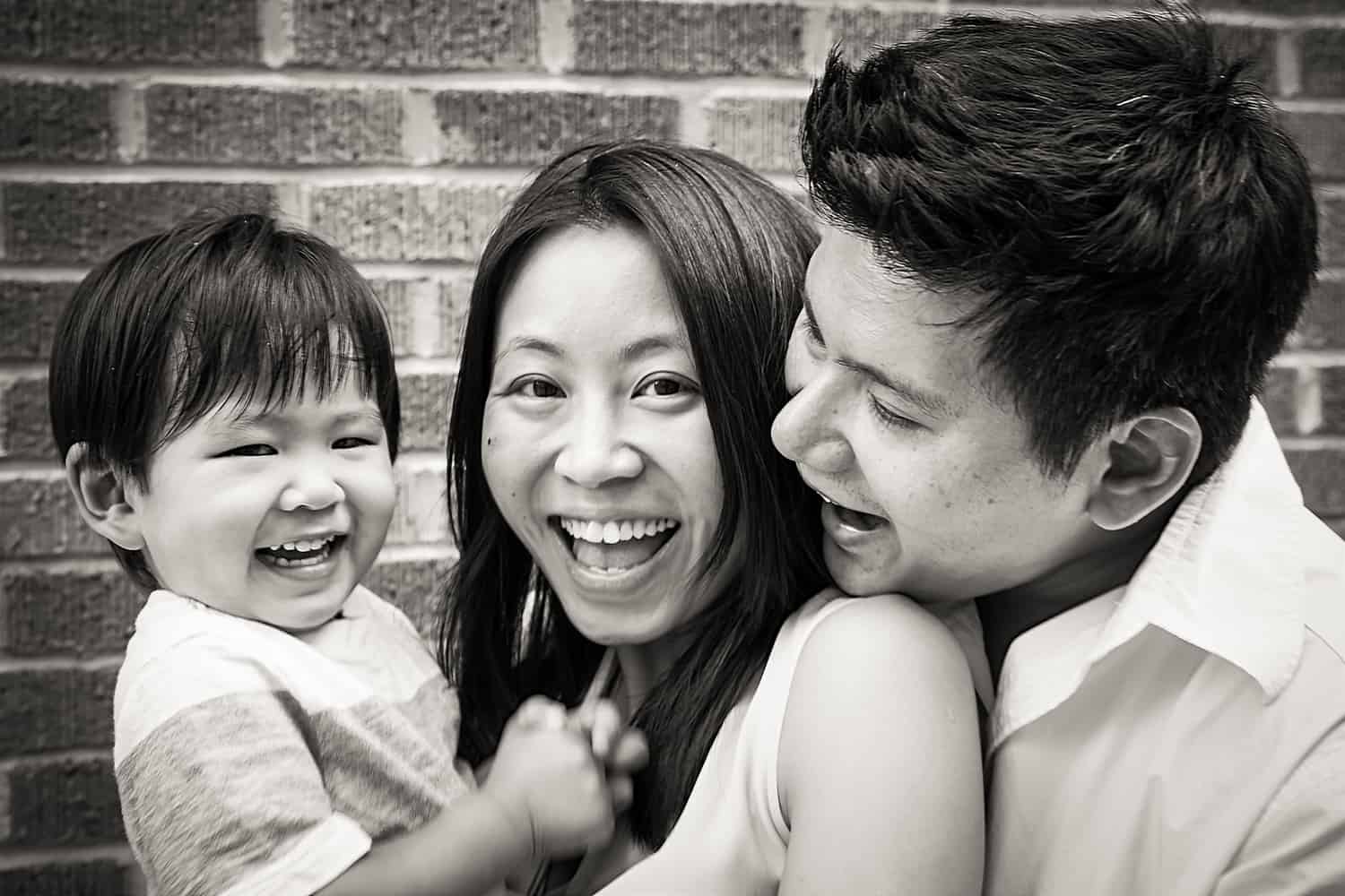 Black and white photo of parents and child in front of brick wall