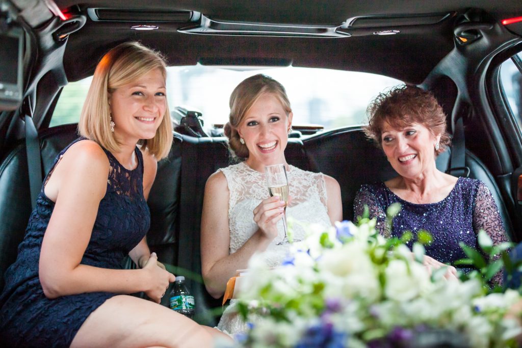 Bride and two women in back of limo with glass of champagne