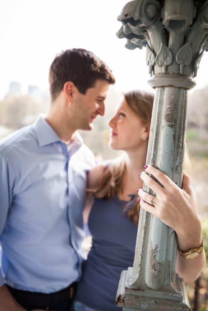Woman's hand with engagement ring on column with couple out of focus in background