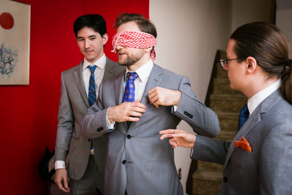 Blindfolded groom and two groomsmen before wedding