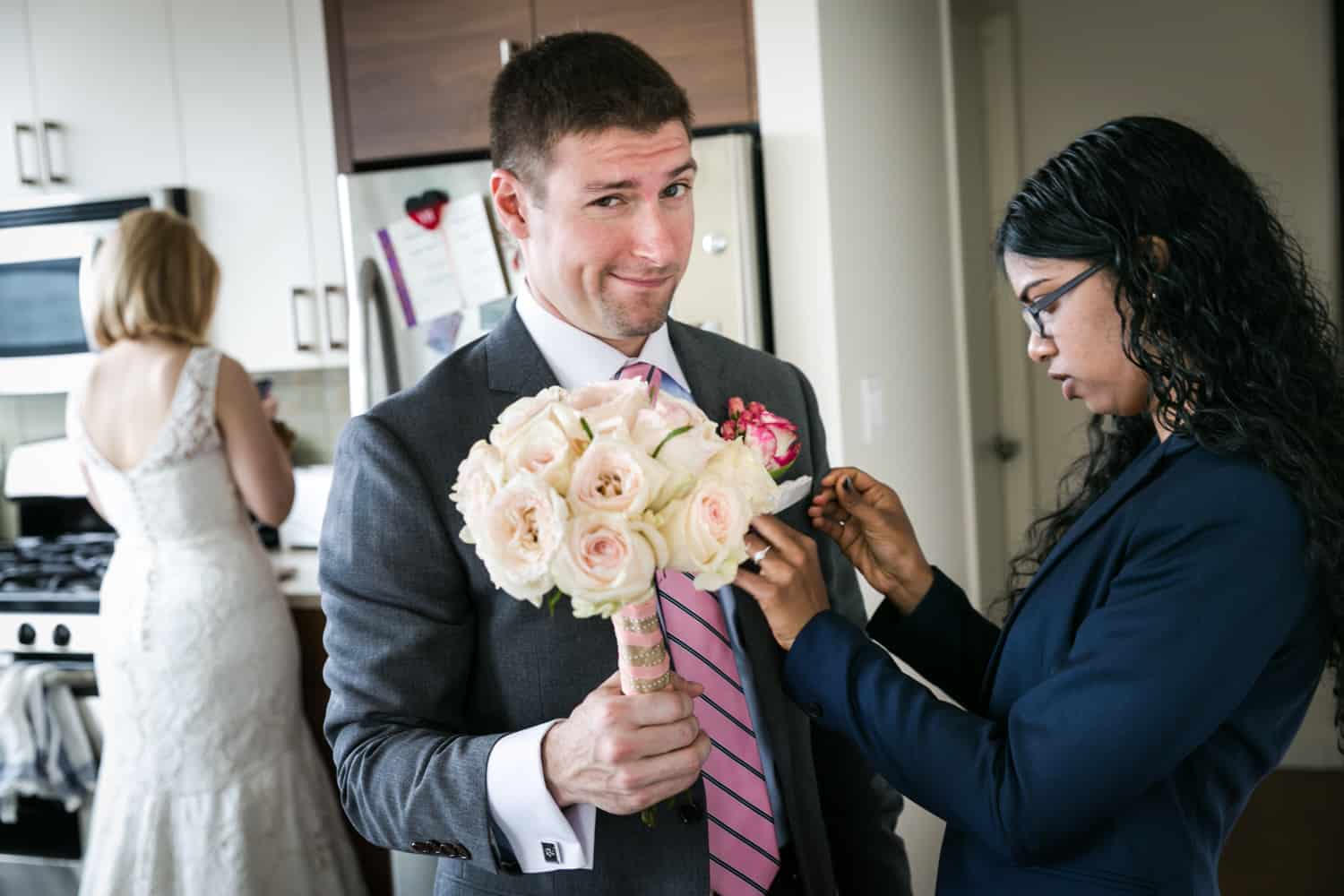 Groom holding bride's bouquet and having pocket square adjusted