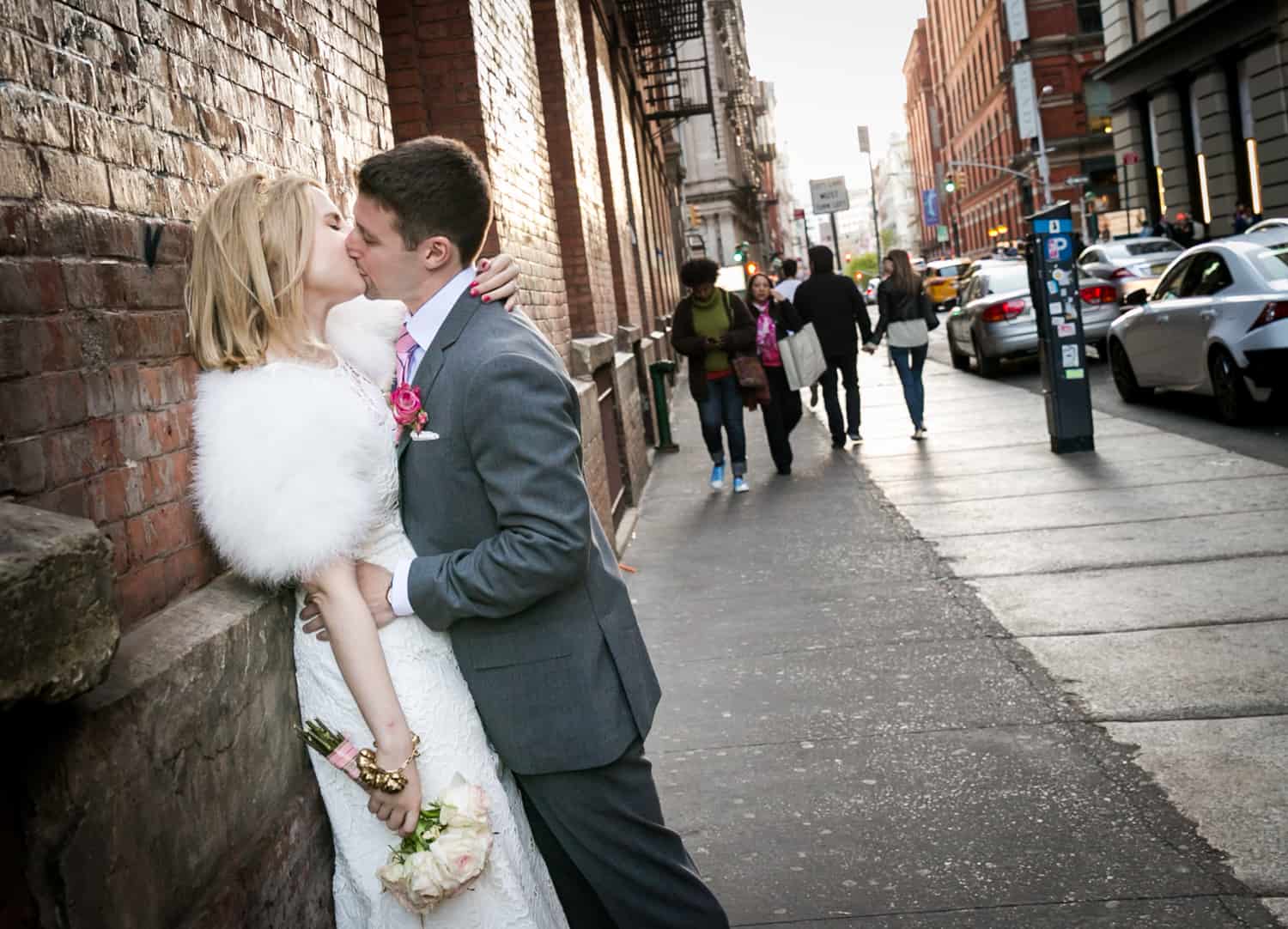 Bride and groom kissing against brick wall in Soho