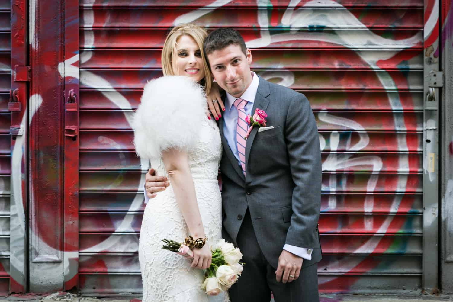 Bride and groom hugging in front of graffiti covered metal gate