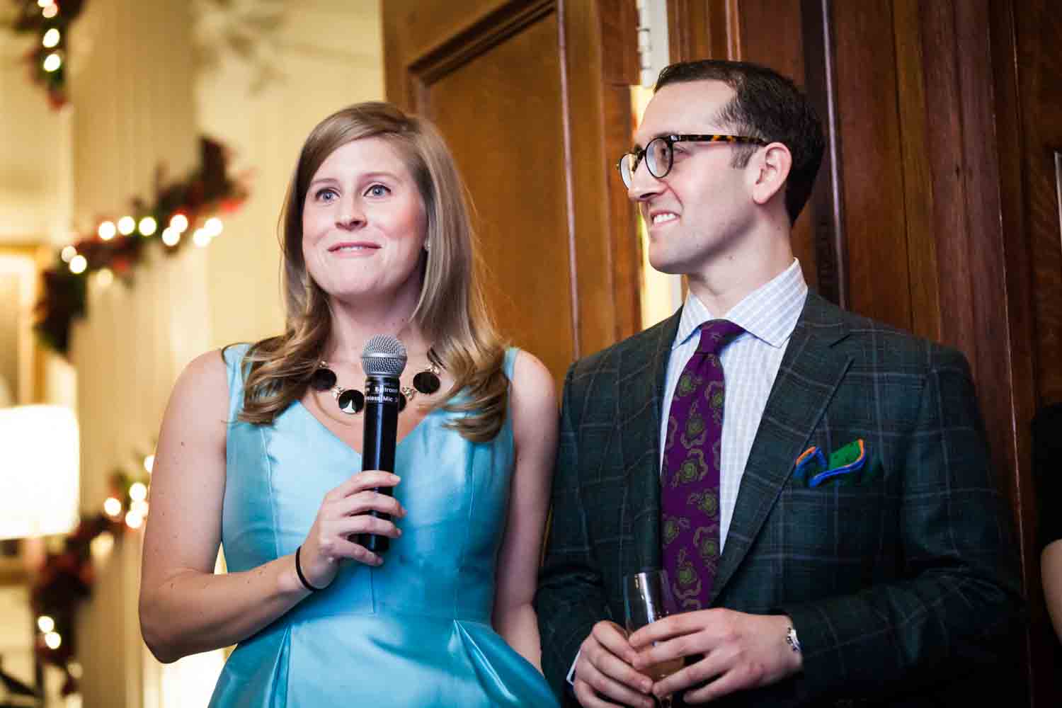 Woman in blue dress holding microphone next to man at a Lotos Club engagement party