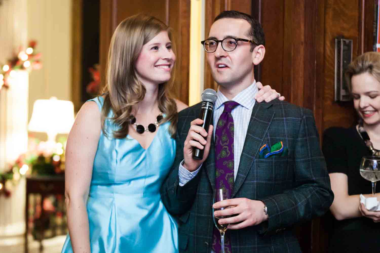 Man speaking into microphone and woman wearing blue dress at a Lotos Club engagement party