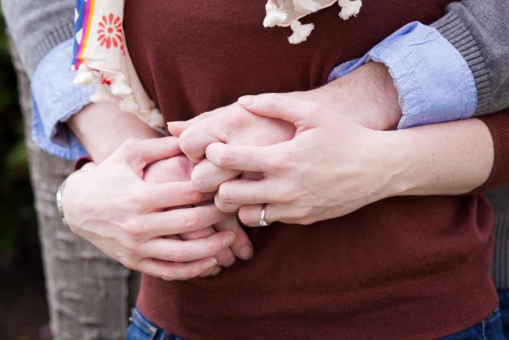 Close up of a couple holding hands with woman wearing engagement ring