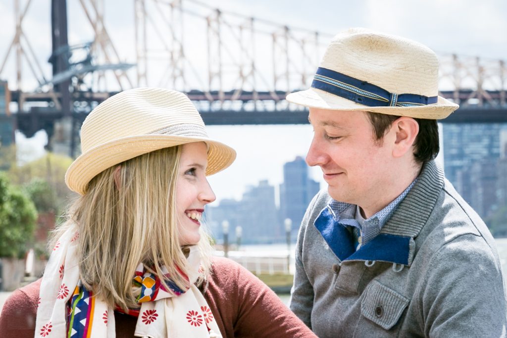 Couple wearing hats and looking at each other with Queensborough Bridge in background