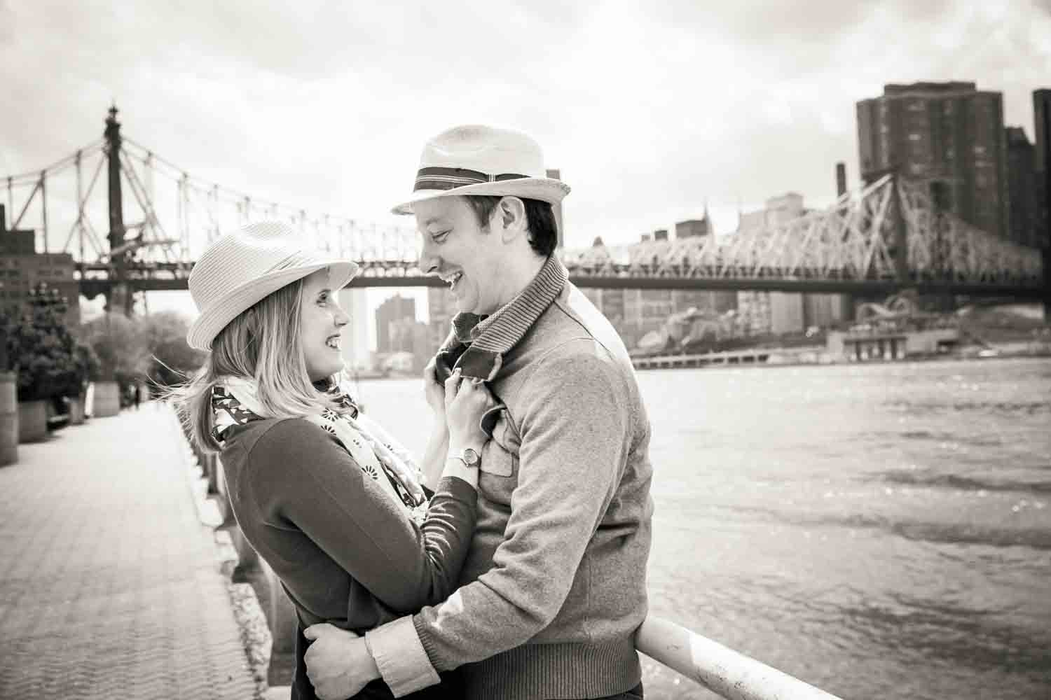 Black and white photo of couple wearing hats and looking at each other with Queensborough Bridge in background