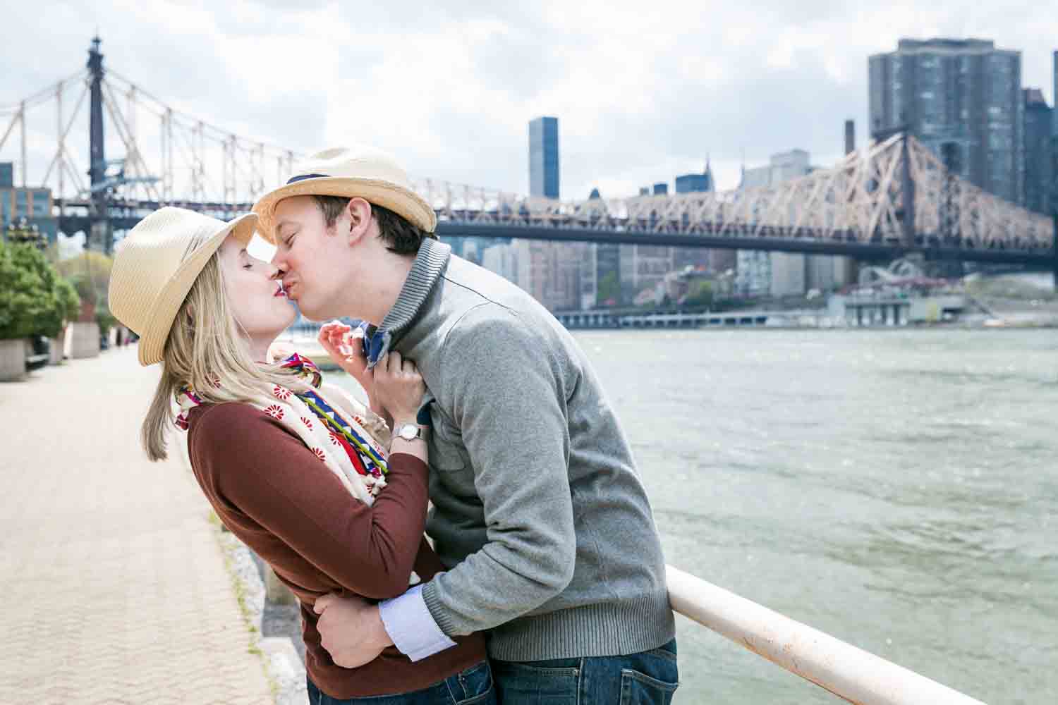Couple kissing against railing with Queensborough Bridge in background