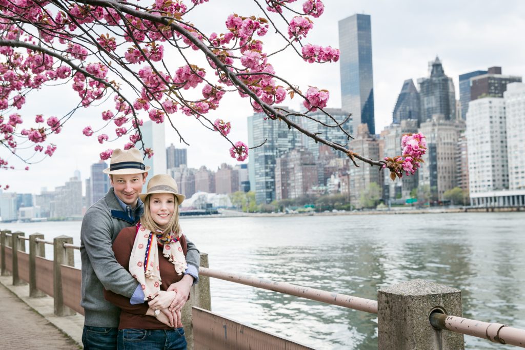 Couple hugging with cherry blossom branches overhead during a Roosevelt Island engagement portrait session