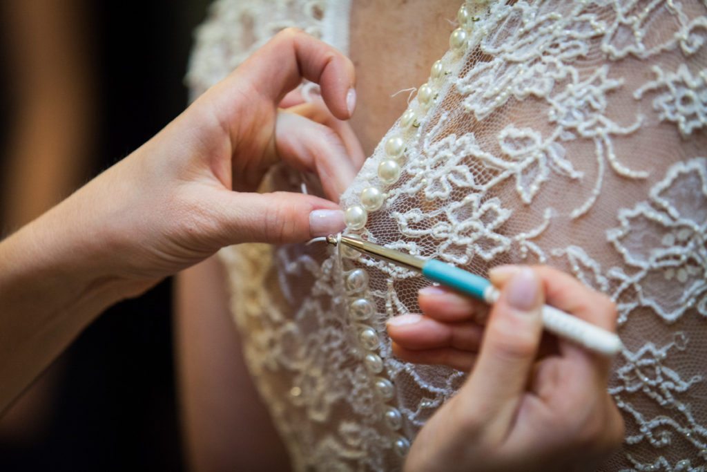 Hands using crochet hook from photographer emergency bag to close buttons on wedding dress