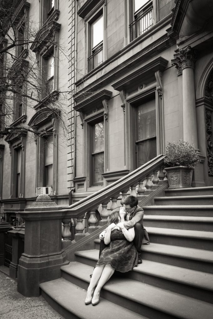 Black and white photo of couple kissing on steps of brownstone