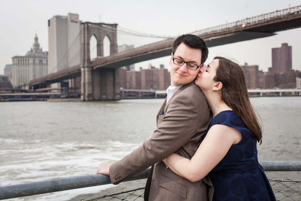 Brooklyn Promenade engagement photos of woman hugging man from behind with Brooklyn Bridge in background