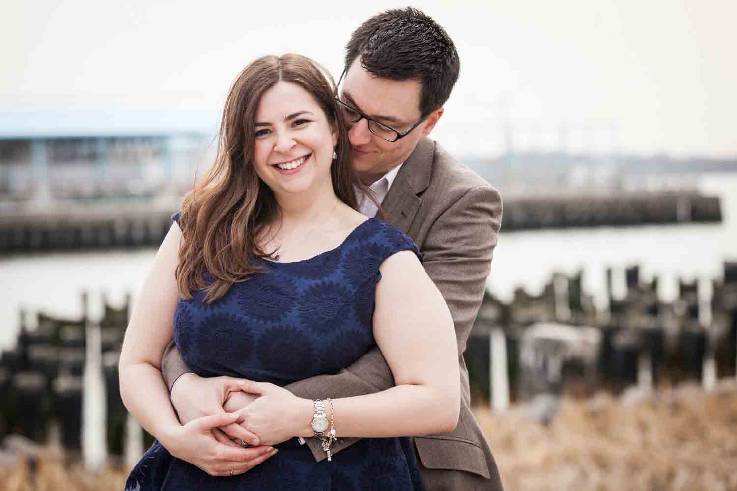 Brooklyn Promenade engagement photos of couple hugging with abandoned dock in background