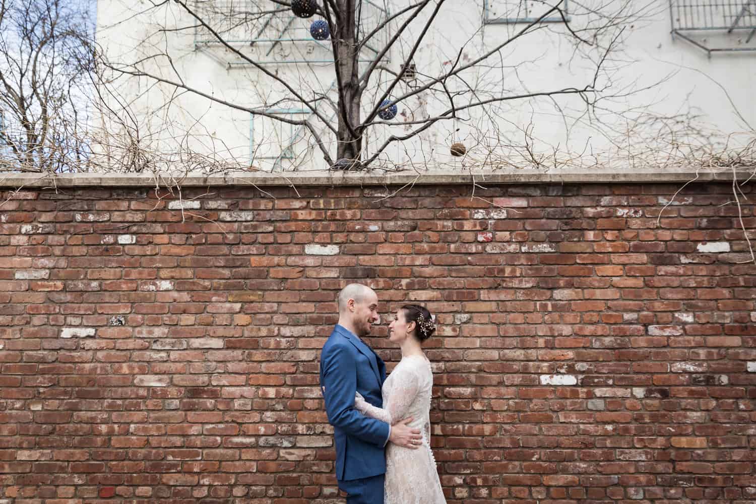 Bride and groom hugging in front of brick wall for an article on what is wedding photojournalism