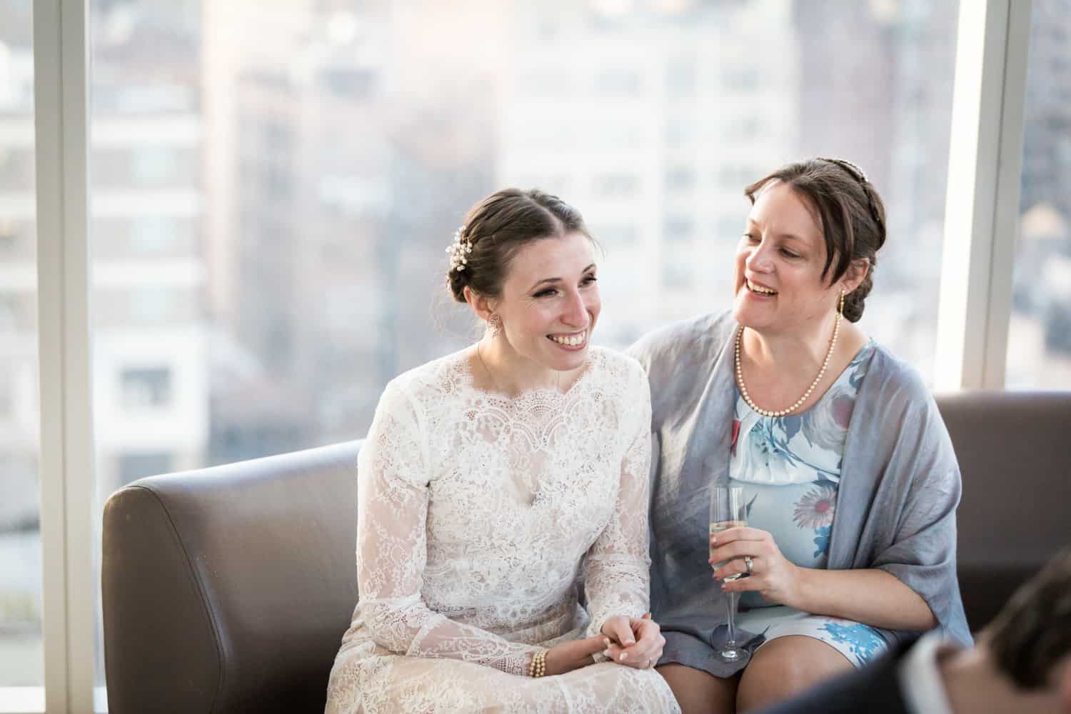 Bride and bridesmaid chatting on couch for an article on what is wedding photojournalism