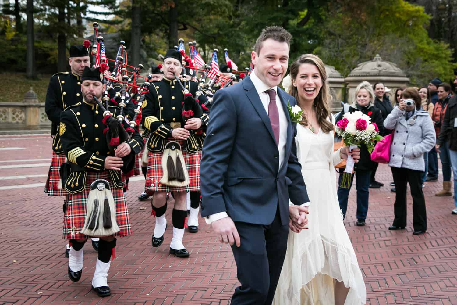 Bride and groom in front of Scottish marching band at a Bethesda Fountain wedding in Central Park