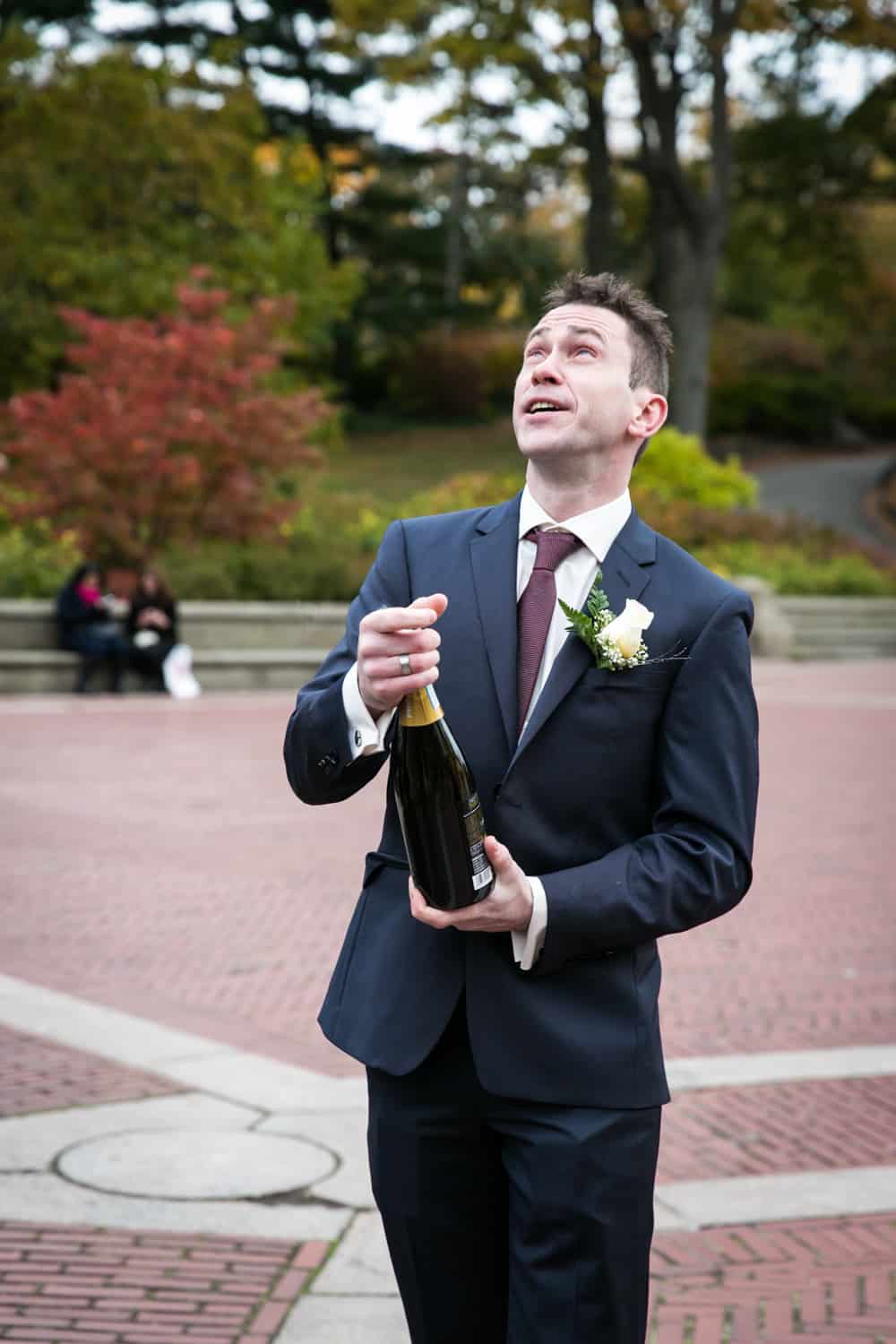 Groom opening champagne bottle at a Bethesda Fountain wedding in Central Park