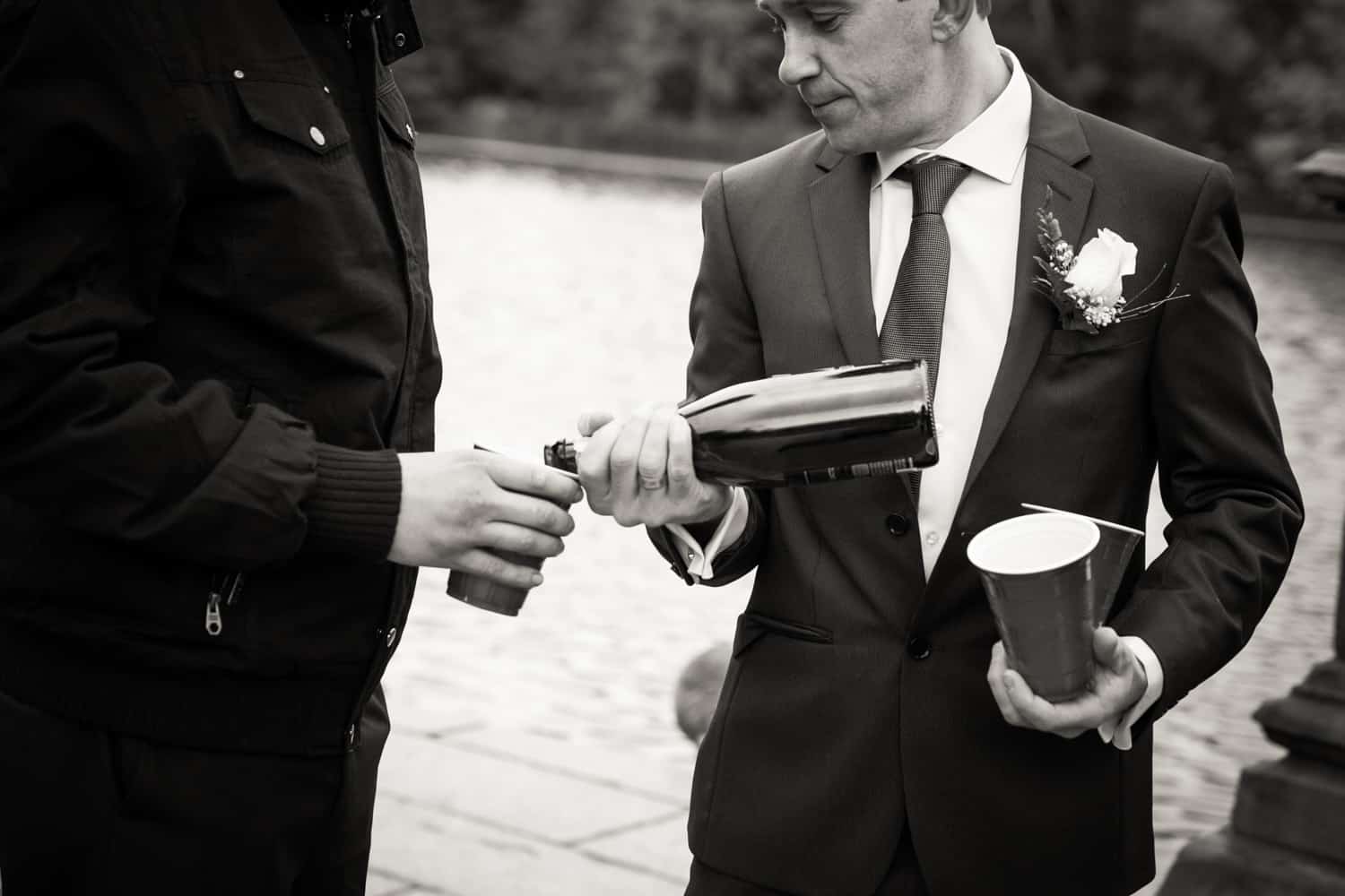 Black and white photo of groom pouring bottle of champagne
